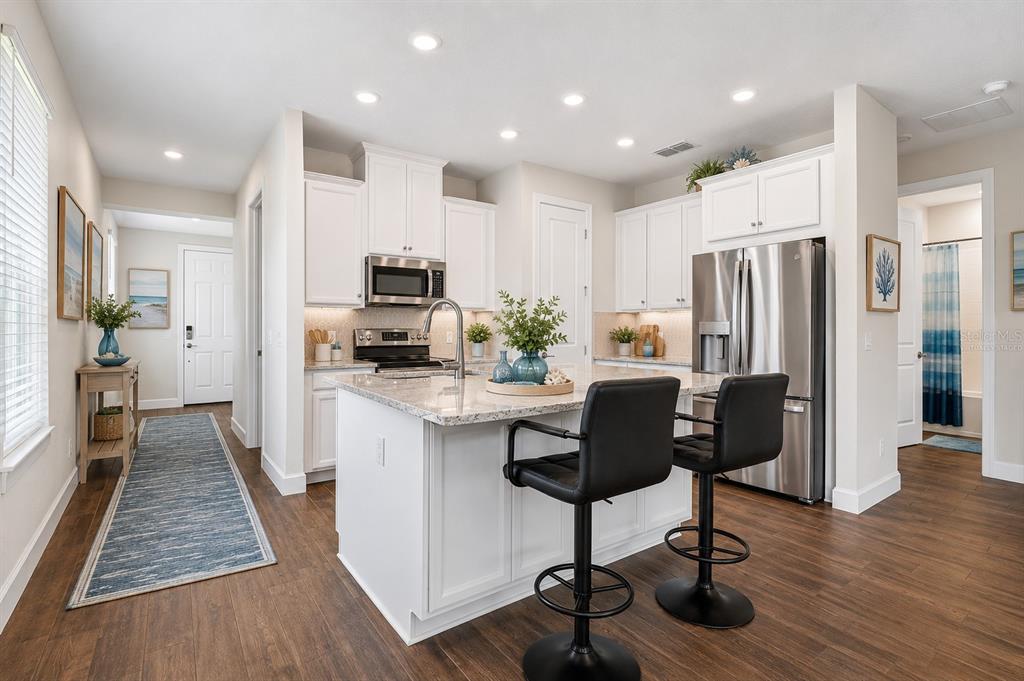 A kitchen with white cabinets and a quartz island overlooks a dining and living area — 1132 VIA GALUPPI STREET, KISSIMMEE, FL