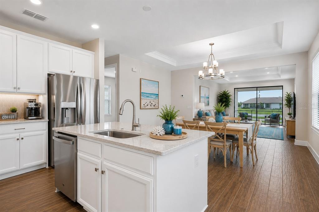 A modern kitchen features white cabinets, granite countertops, a central island, and stainless steel appliances — 1132 VIA GALUPPI STREET, KISSIMMEE, FL