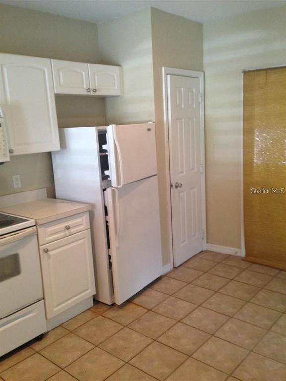 A kitchen features white cabinets, a white refrigerator, a white stove, and tiled flooring — 4214 PLANTATION COVE DRIVE, ORLANDO, FL