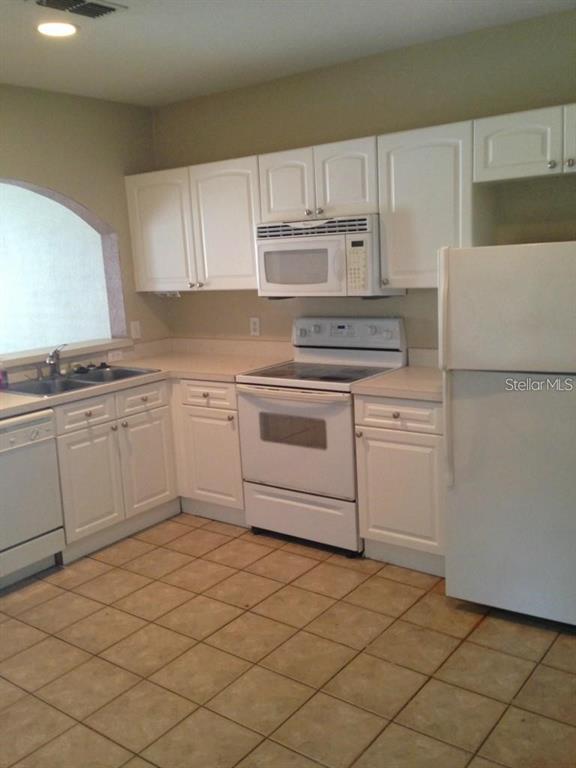 A kitchen features white cabinets, white appliances, and light-colored tile flooring — 4214 PLANTATION COVE DRIVE, ORLANDO, FL