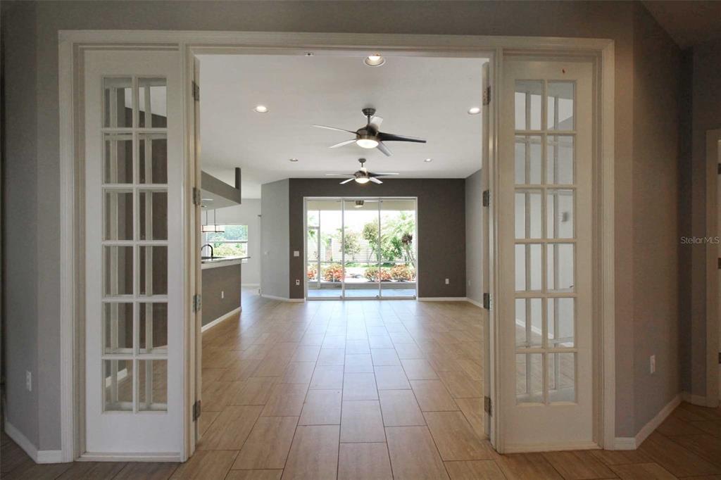 A view through French doors into an open-concept living area with tile flooring and ceiling fans — 4815 77TH STREET E, BRADENTON, FL