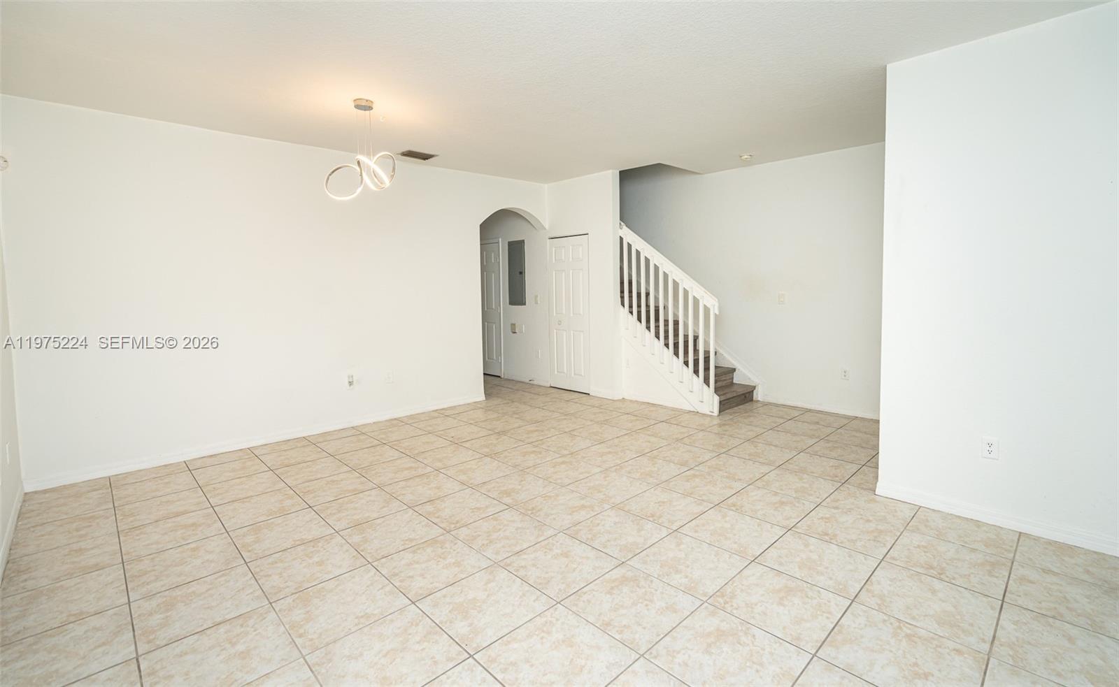 An empty room with beige tile flooring, white walls, a staircase, and a modern light fixture — 14046 SW 49th St # 16, Miramar FL 33027, MIRAMAR, FL