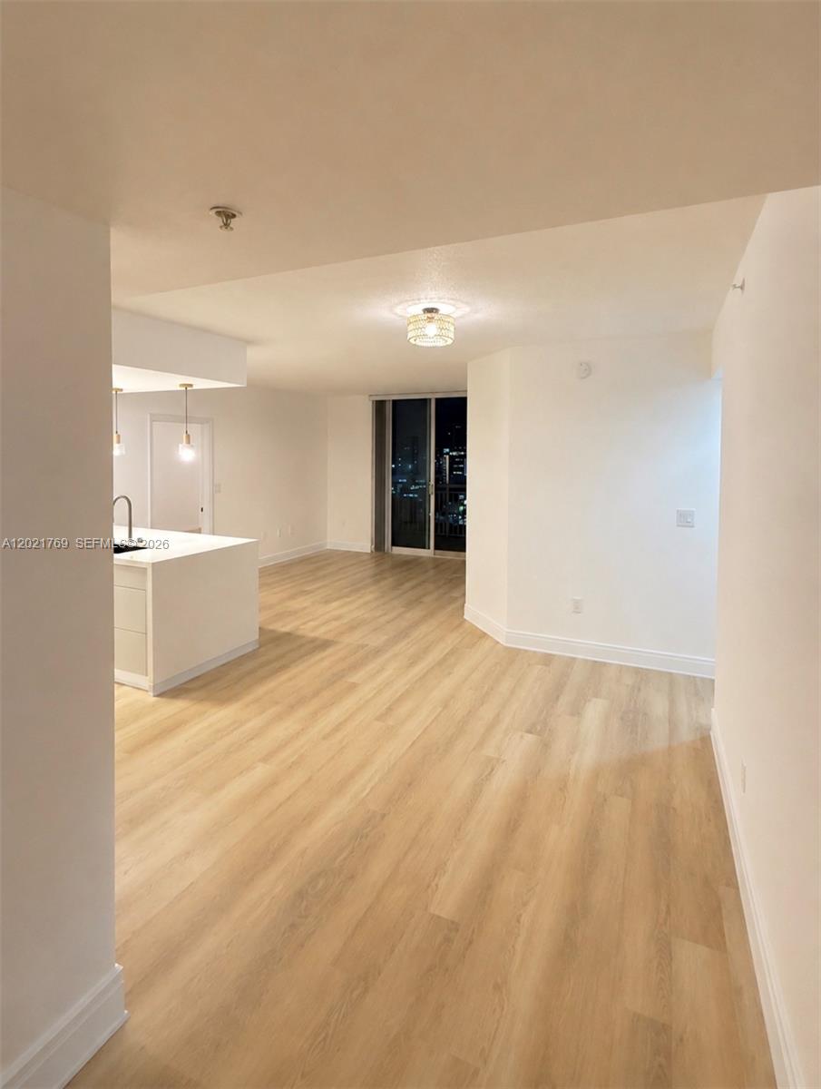 An open-concept living area features light wood-look flooring, white walls, and a kitchen island — 275 NE 18th St # 910, Miami FL 33132, MIAMI, FL
