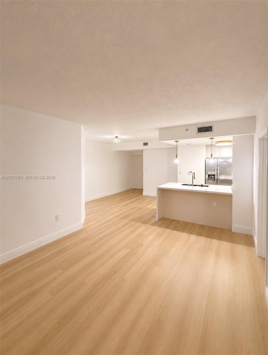 An open-concept living area features light wood-look flooring and a kitchen with a white island — 275 NE 18th St # 910, Miami FL 33132, MIAMI, FL