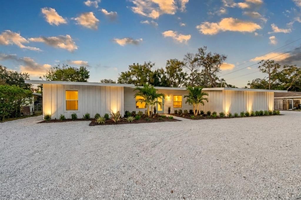 A single-story white house with vertical siding, a gravel driveway, and palm trees at dusk — 2069 BOUGAINVILLEA STREET, SARASOTA, FL