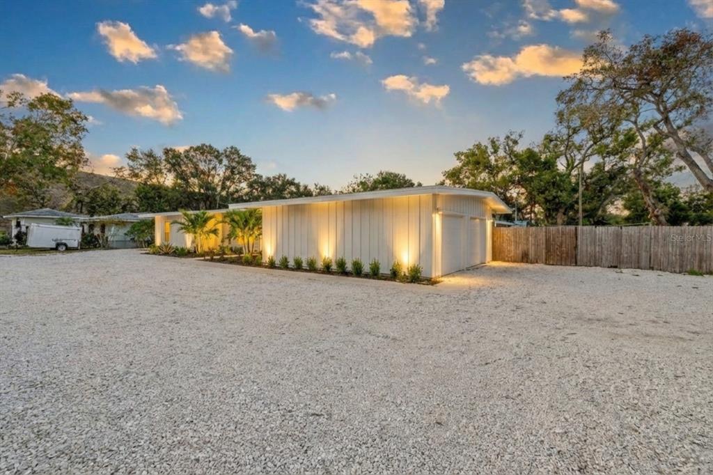 A white mid-century modern house with a gravel driveway and exterior uplighting at dusk — 2069 BOUGAINVILLEA STREET, SARASOTA, FL