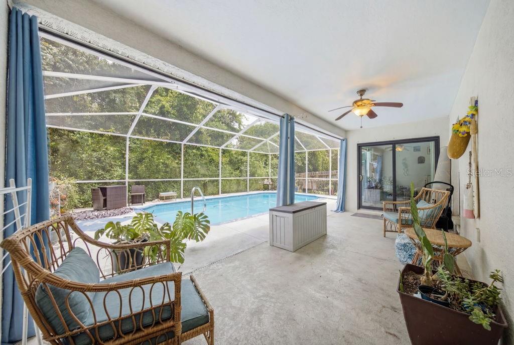 A covered patio features a swimming pool with a screen enclosure and wicker furniture — 10249 RAINBOW OAKS DRIVE, HUDSON, FL
