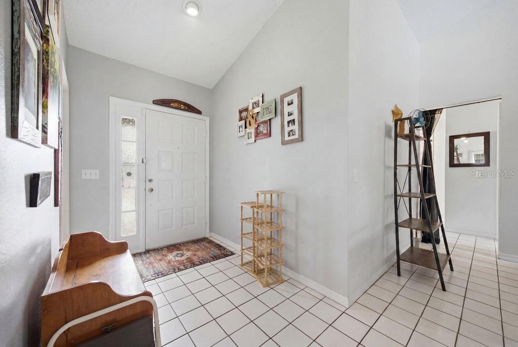 An entryway features a white front door, tiled flooring, a wooden bench, and wall decor — 10249 RAINBOW OAKS DRIVE, HUDSON, FL
