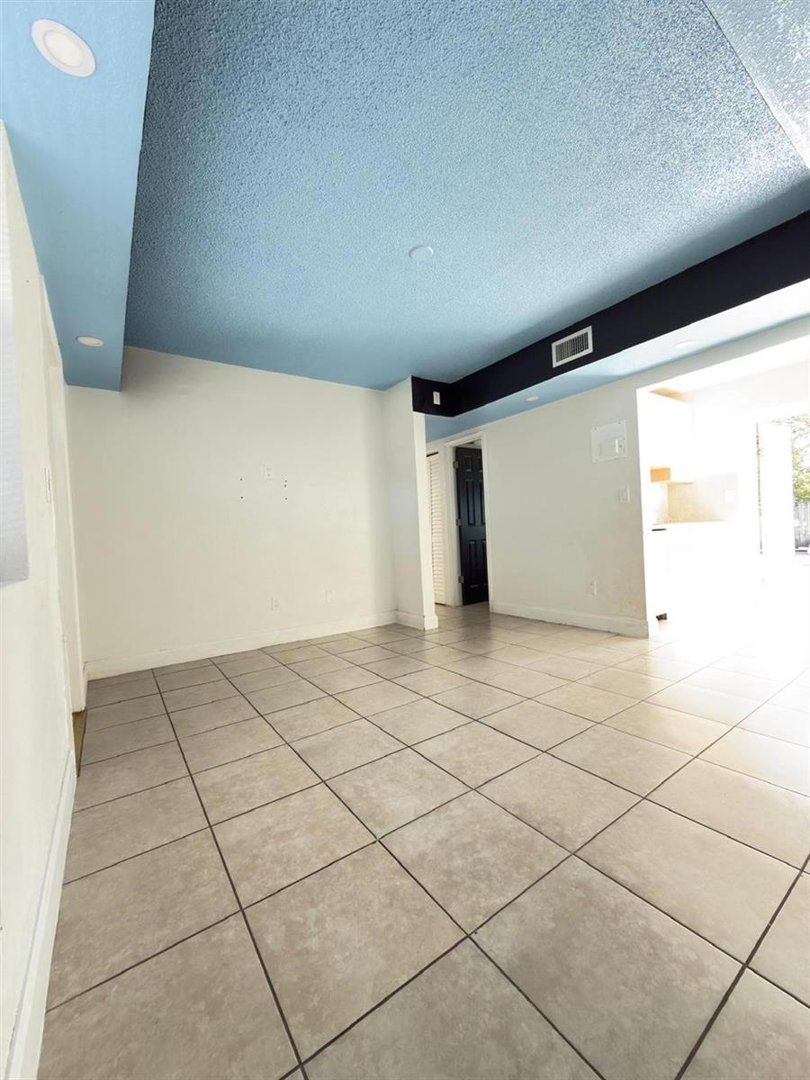 An empty room features light blue textured ceilings, white walls, and beige tiled flooring — 1832 NE 49th Street, Pompano Beach FL 33064, POMPANO BEACH, FL