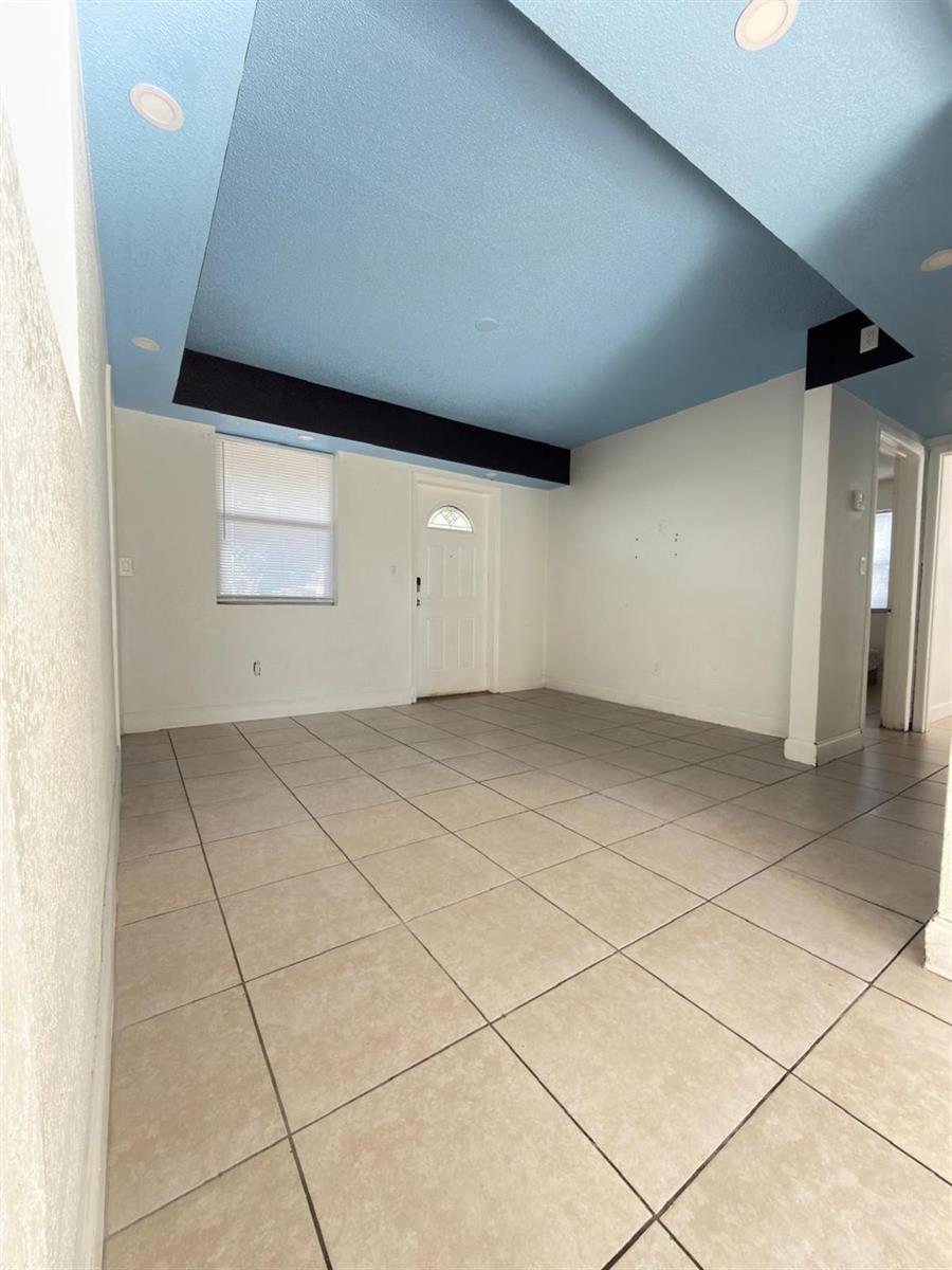 An empty room with light-colored tile flooring and a blue tray ceiling — 1832 NE 49th Street, Pompano Beach FL 33064, POMPANO BEACH, FL