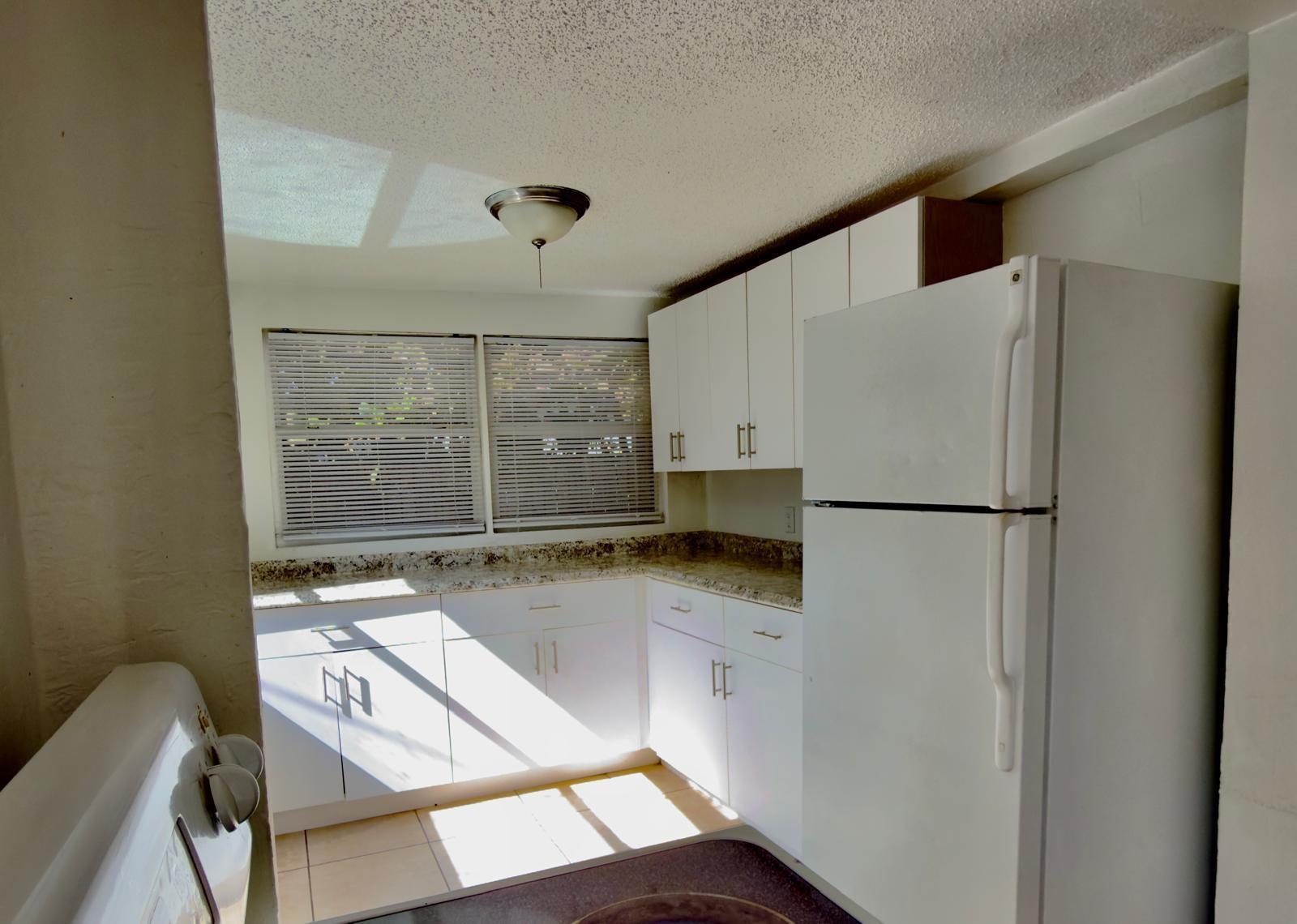 A kitchen features white cabinetry, granite countertops, a white refrigerator, and two windows with blinds — 1832 NE 49th Street, Pompano Beach FL 33064, POMPANO BEACH, FL