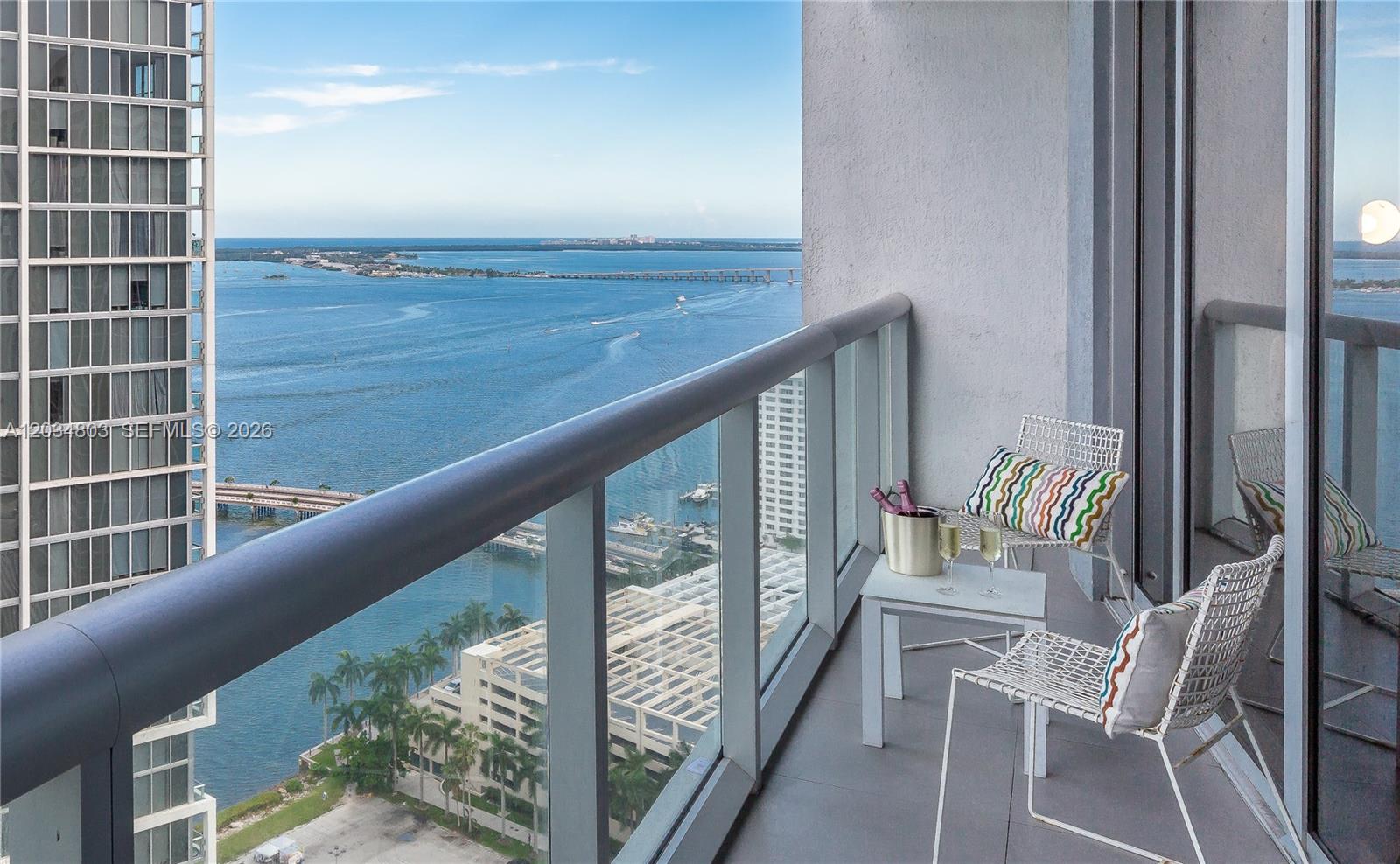 A high-rise balcony with two chairs, a small table, and a view of the water — 485 Brickell Ave # 3211, Miami FL 33131, MIAMI, FL