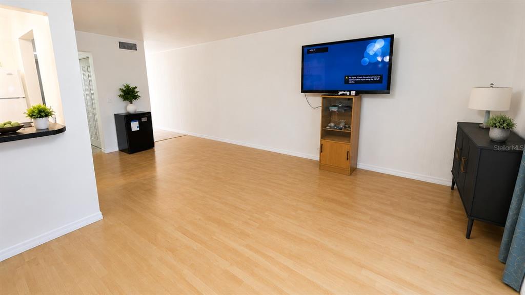 A living room with light wood flooring, a wall-mounted television, and a black storage cabinet — 1500 VIRGINIA AVENUE UNIT 209, DAYTONA BEACH, FL