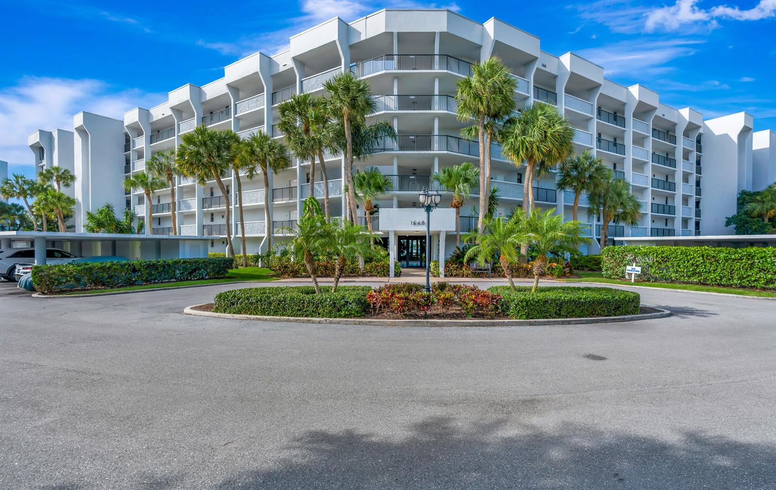 A multi-story white apartment building features a circular driveway and palm trees in front — 1648 Jupiter Cove Drive # 608b, Jupiter FL 33469, JUPITER, FL