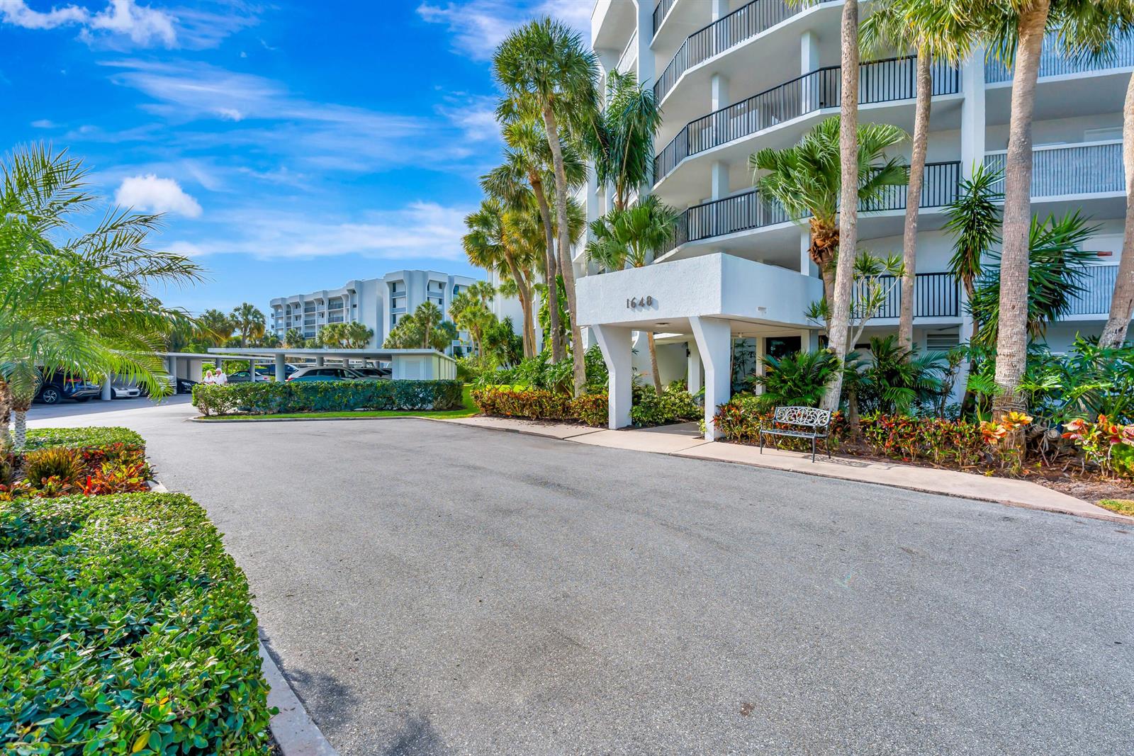 A multi-story white apartment building features a covered entrance with palm trees and landscaping — 1648 Jupiter Cove Drive # 608b, Jupiter FL 33469, JUPITER, FL