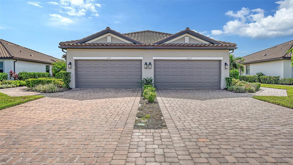 A duplex home features two gray garage doors and a shared paver driveway — 6223 PLATEAU COURT, BRADENTON, FL