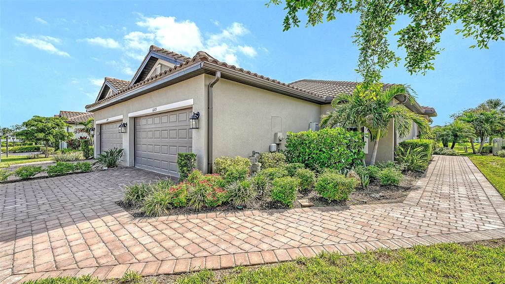 A beige house with a two-car garage and a paved driveway surrounded by landscaping — 6223 PLATEAU COURT, BRADENTON, FL