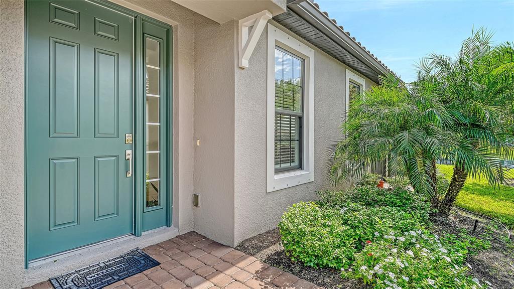 A teal front door with a side light stands beside a window and palm tree — 6223 PLATEAU COURT, BRADENTON, FL