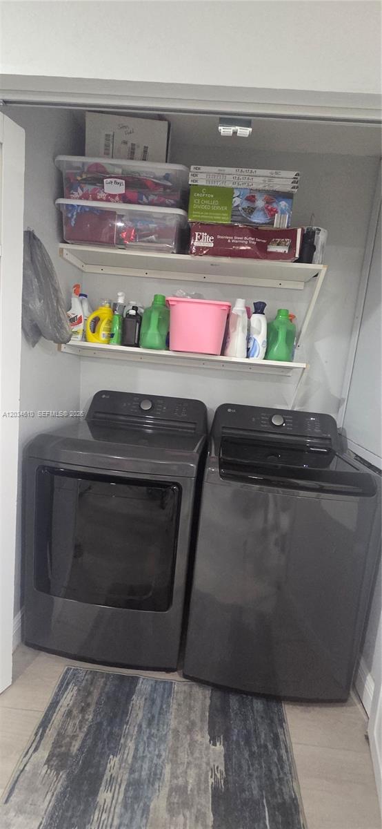A laundry closet features a stacked washer and dryer beneath two shelves holding cleaning supplies and storage bins — NORTH LAUDERDALE, FL