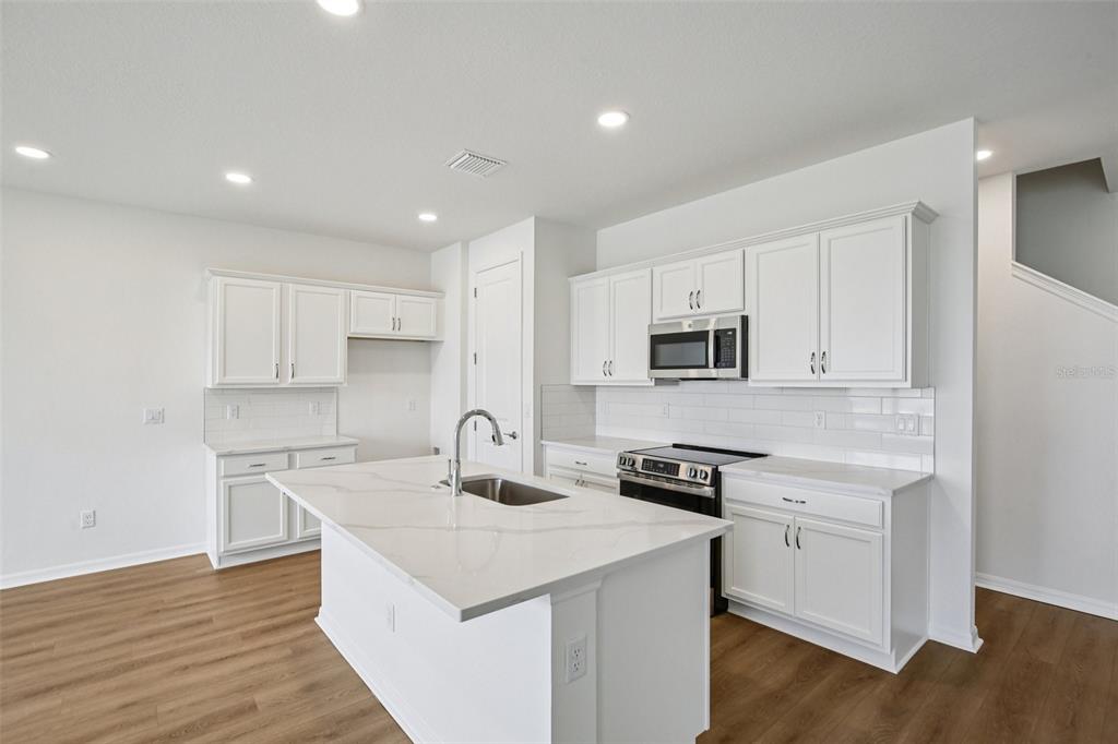 A modern kitchen with white cabinets, a central island, and light wood-look flooring — 31481 SPANISH MISSION ROAD, SAN ANTONIO, FL