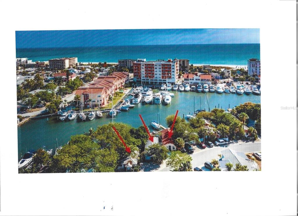 An aerial view shows waterfront homes and a marina with boats near a beach — 249 BOCA CIEGA DRIVE, MADEIRA BEACH, FL