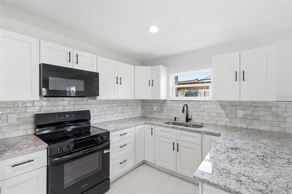 A kitchen with white cabinets, granite countertops, a black stove, and a subway tile backsplash — 311 12TH STREET W, PALMETTO, FL