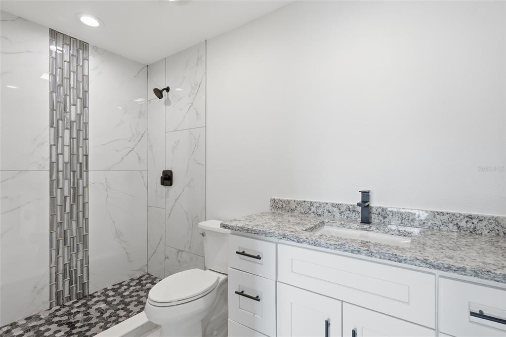 A bathroom features a white vanity with granite countertops, a toilet, and a tiled shower — 311 12TH STREET W, PALMETTO, FL