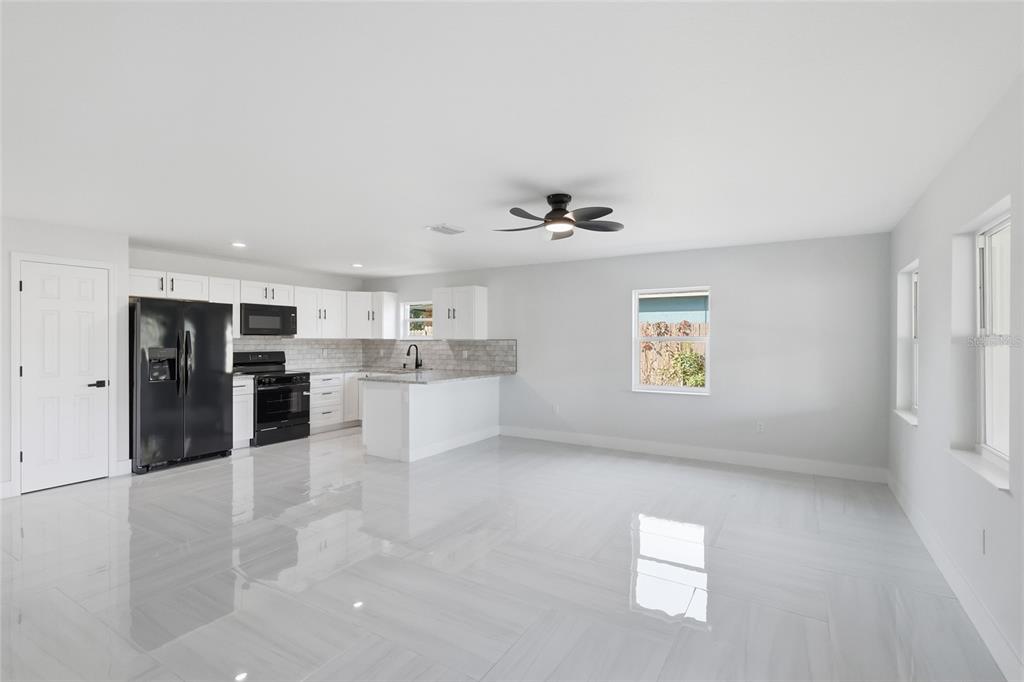 A bright, open-concept kitchen and living area features white cabinetry, black appliances, and tiled flooring — 311 12TH STREET W, PALMETTO, FL