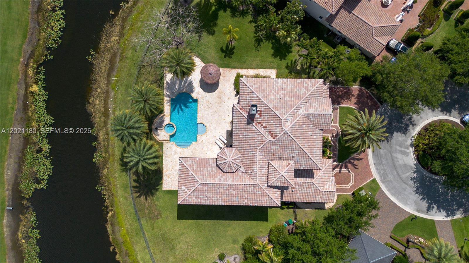 An aerial view shows a house with a tiled roof, pool, and patio beside a canal — 7290 Lemon Grass Dr, Parkland FL 33076, PARKLAND, FL