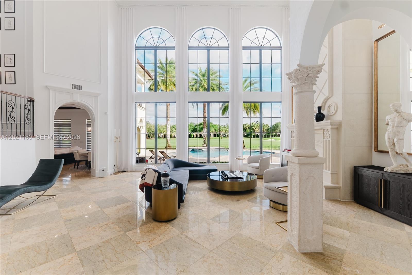 A spacious living room features tall arched windows, marble floors, and a view of a pool — 7290 Lemon Grass Dr, Parkland FL 33076, PARKLAND, FL
