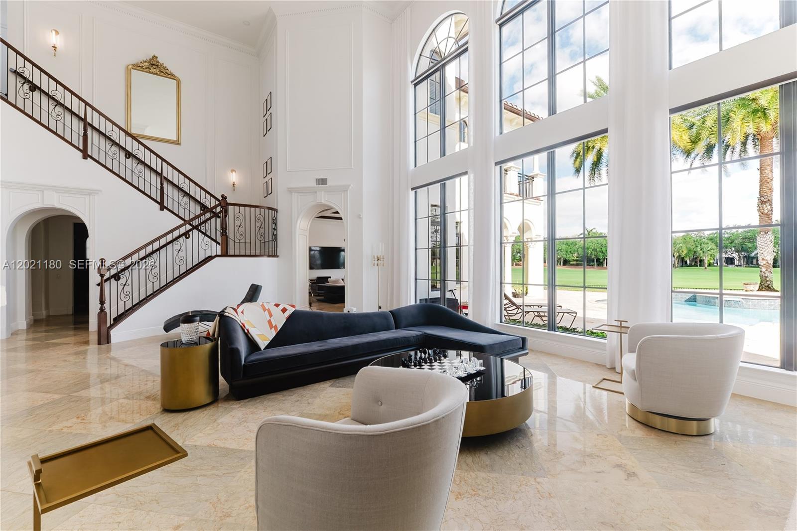 A spacious living room features a grand staircase, floor-to-ceiling windows, and modern furniture — 7290 Lemon Grass Dr, Parkland FL 33076, PARKLAND, FL