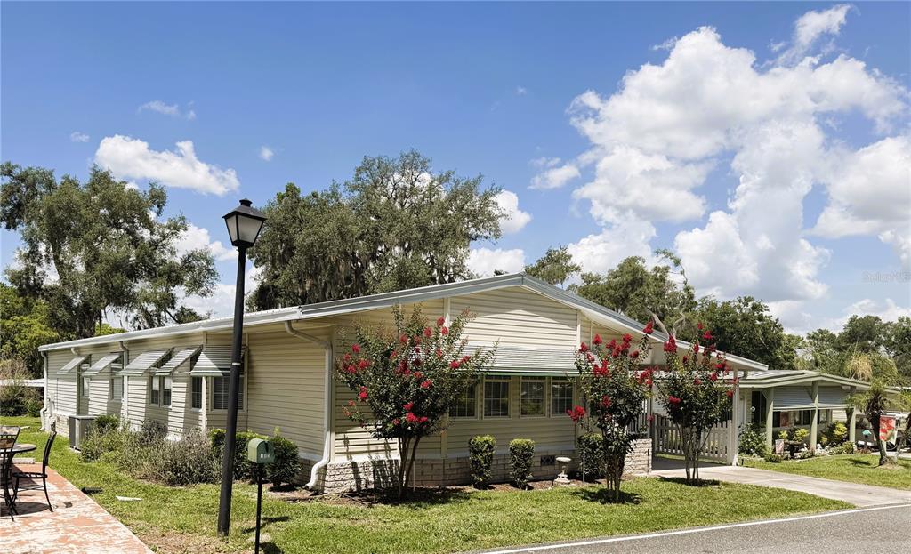A single-story mobile home with light siding, green awnings, and flowering trees in the yard — 103 ORCHID WAY, LEESBURG, FL