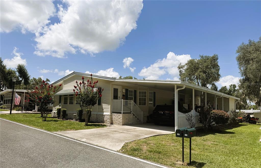 A single-story manufactured home with a carport, concrete driveway, and a small front lawn — 103 ORCHID WAY, LEESBURG, FL