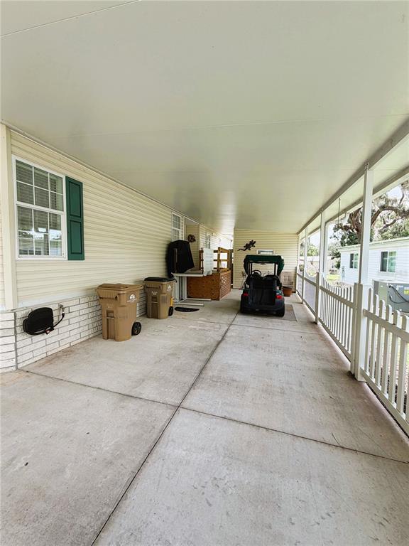 A concrete carport features a golf cart, two trash bins, and a white picket fence — 103 ORCHID WAY, LEESBURG, FL