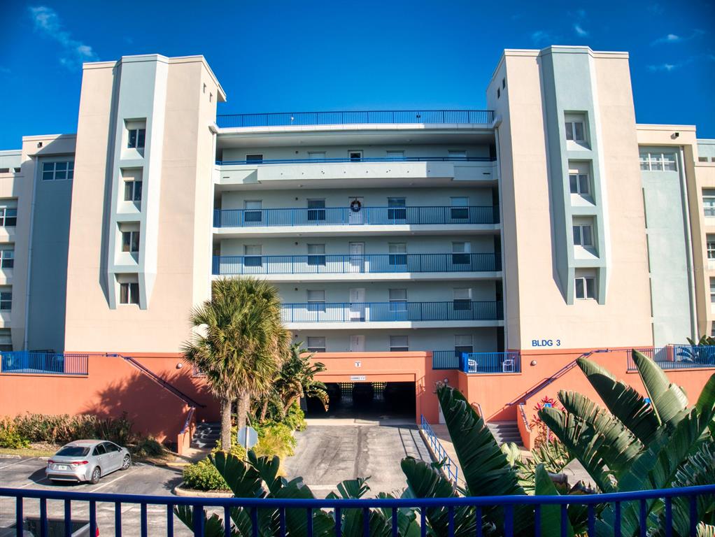 The exterior of a multi-story apartment building features balconies, a ground-level parking garage, and landscaping — 5300 S ATLANTIC AVENUE UNIT 3502, NEW SMYRNA BEACH, FL