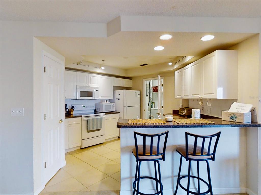 A kitchen with white cabinets, a breakfast bar with two stools, and tile flooring — 5300 S ATLANTIC AVENUE UNIT 3502, NEW SMYRNA BEACH, FL