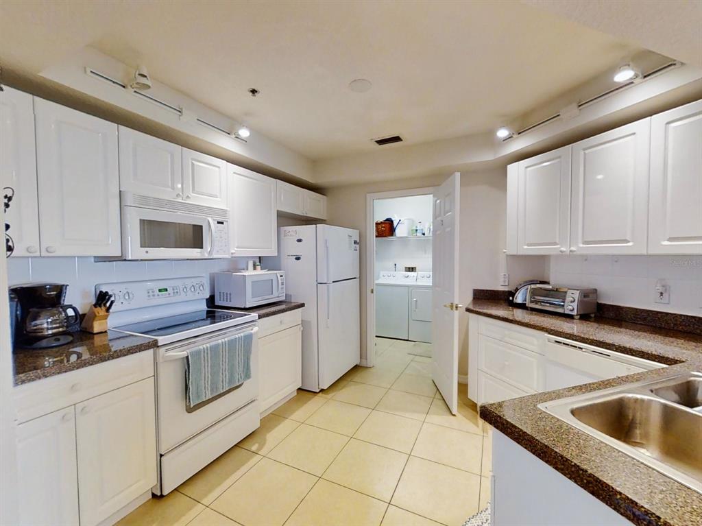 A kitchen with white cabinets, granite countertops, white appliances, and a doorway to a laundry area — 5300 S ATLANTIC AVENUE UNIT 3502, NEW SMYRNA BEACH, FL