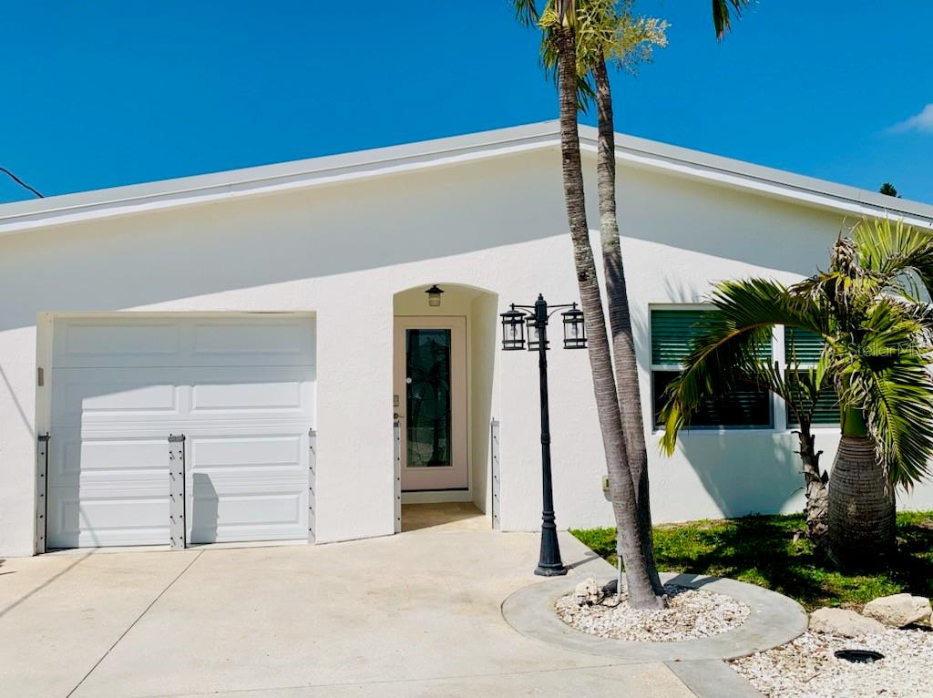 A white single-story house exterior with a garage, front door, and a palm tree — 14162 W PARSLEY DRIVE, MADEIRA BEACH, FL