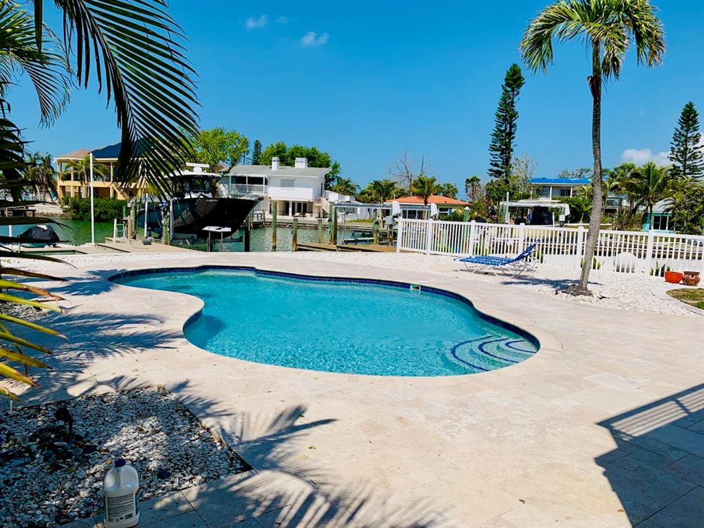 A swimming pool with a stone deck sits in a backyard overlooking a canal and boat — 14162 W PARSLEY DRIVE, MADEIRA BEACH, FL