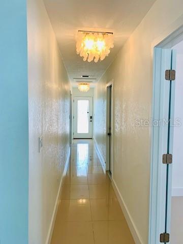 A hallway with light-colored walls, tile flooring, and two decorative light fixtures leads to a door — 14162 W PARSLEY DRIVE, MADEIRA BEACH, FL