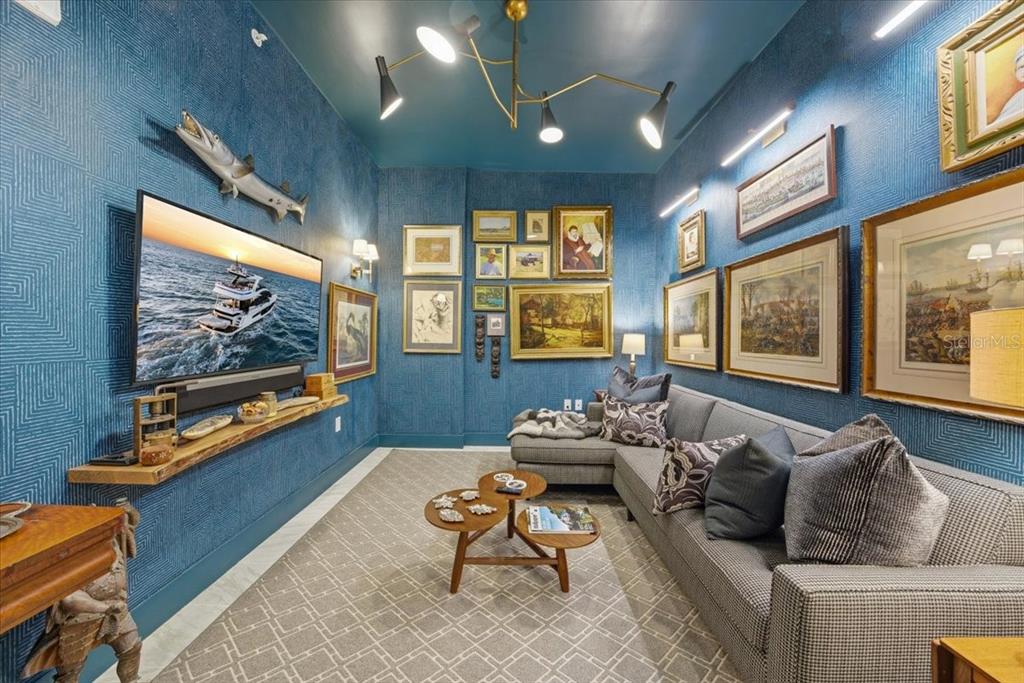 A blue-walled media room features a mounted television, gallery wall, sectional sofa, and chandelier — 777 3RD AVENUE N UNIT 1606, ST PETERSBURG, FL