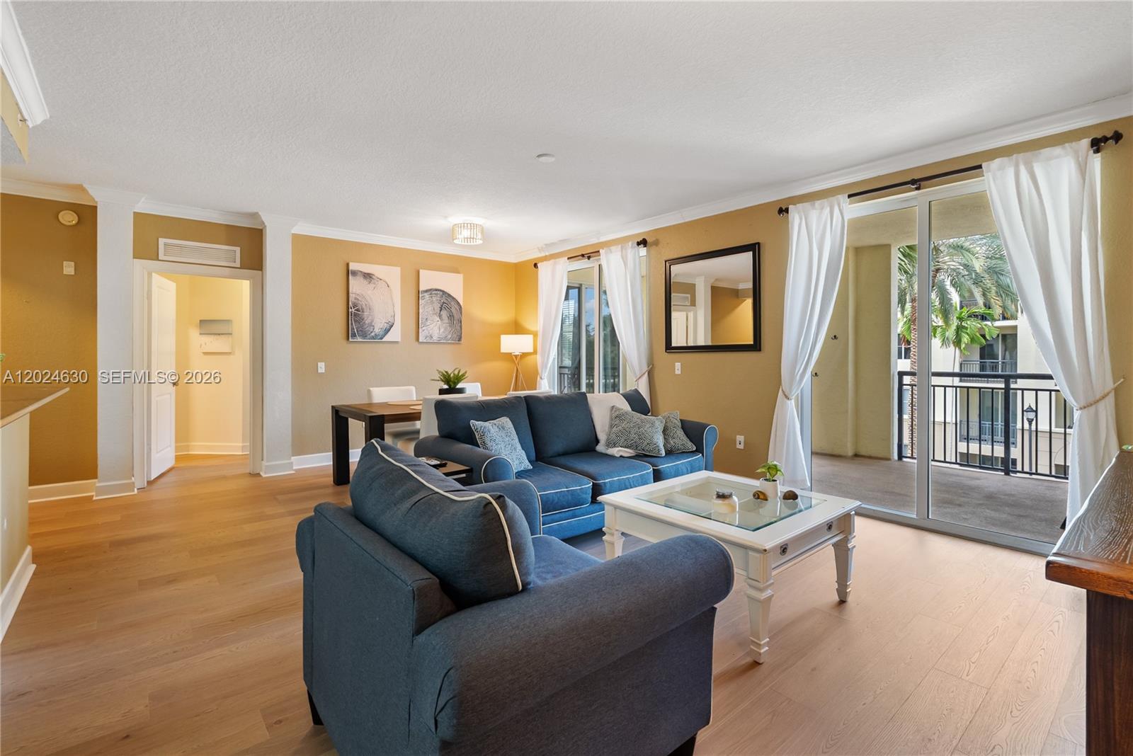 A living room features blue sofas, a white coffee table, and a balcony with palm trees — 2 Renaissance Way # 305, Boynton Beach FL 33426, BOYNTON BEACH, FL