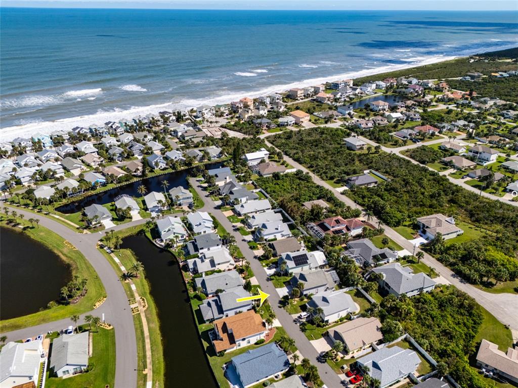 An aerial view shows a coastal neighborhood with houses, a canal, and the ocean — 24 MEDFORD DRIVE, PALM COAST, FL