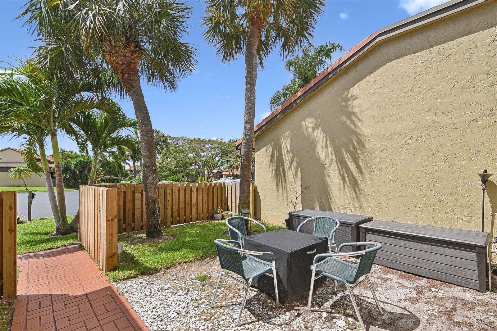 A patio with a table and chairs sits next to a house with palm trees — 11063 Oakdale Road, Boynton Beach FL 33437, BOYNTON BEACH, FL