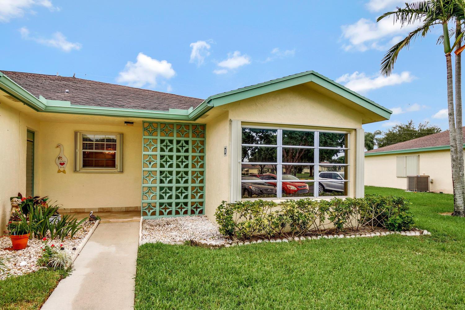 A yellow single-story home features a decorative teal breeze block wall and a large window — 5126 Lakefront Boulevard # D, Delray Beach FL 33484, DELRAY BEACH, FL