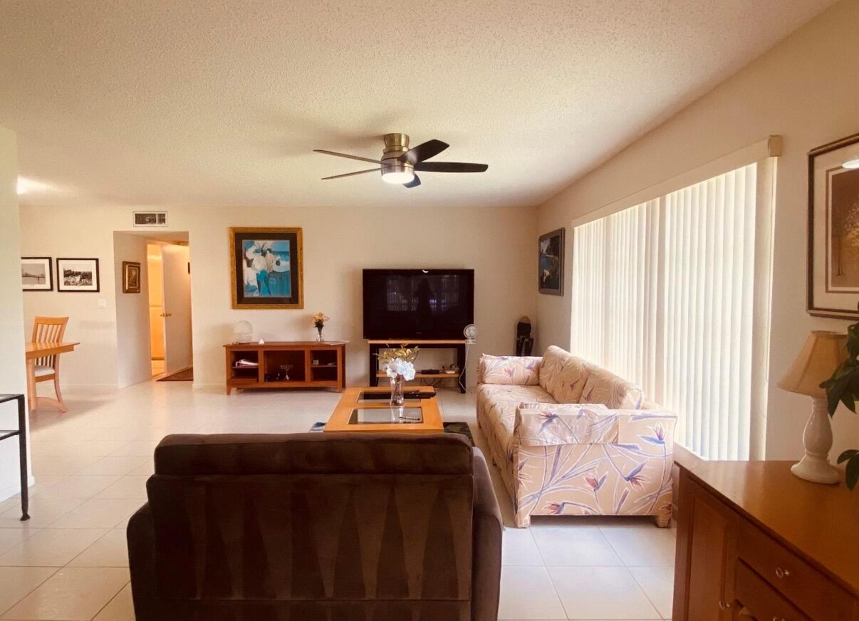 A living room with tile floors, a floral sofa, a television, and a ceiling fan — 5126 Lakefront Boulevard # D, Delray Beach FL 33484, DELRAY BEACH, FL