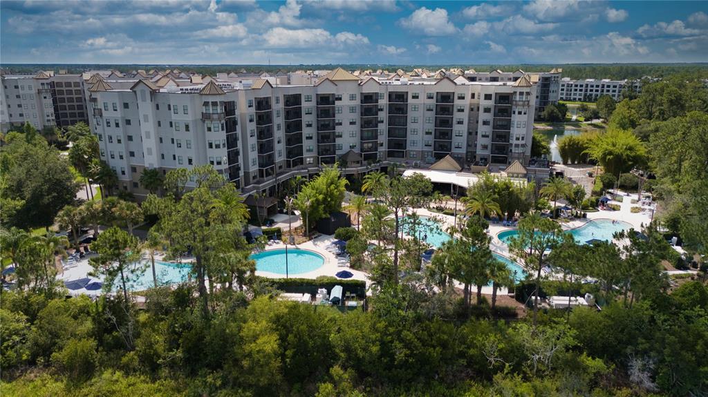 An aerial view of a multi-story apartment complex featuring multiple swimming pools and lush landscaping — 14501 GROVE RESORT AVENUE UNIT 2135, WINTER GARDEN, FL