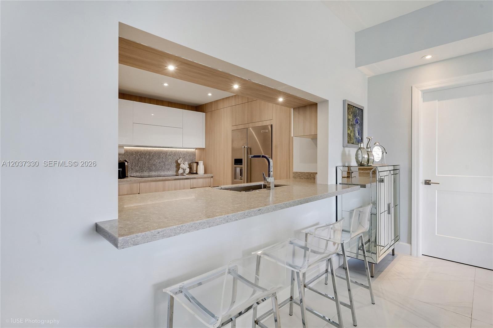 A kitchen with light wood cabinetry and white upper cabinets features a stone breakfast bar — 201 Crandon Blvd # 833, Key Biscayne FL 33149, KEY BISCAYNE, FL