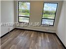 An empty room features light wood-look flooring, white walls, and two windows overlooking greenery — 2001 N Dixie Hwy # 4, Pompano Beach FL 33060, POMPANO BEACH, FL