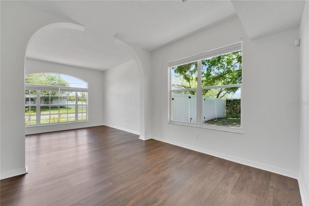 An empty room with dark wood-look flooring, white walls, and an arched entryway — 1101 BLUFIELD AVENUE, BRANDON, FL